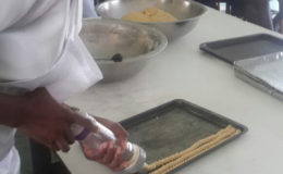 A student pumps out rows of cheese straw dough for baking.