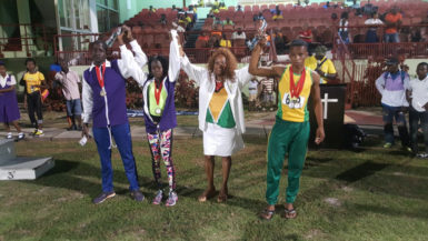 Ira Lewis, popularly known as ‘Lady Ira’ raises the hands of some of the athletes who received racing watches following last night’s National Schools Cycling, Swimming and Track and Field Championships. 