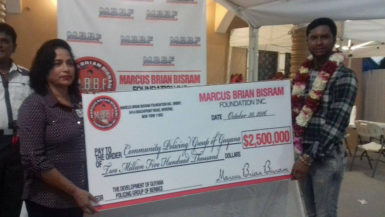 Radica Ramanandan, Community Policing Liaison Officer, Ministry of Public Security receiving the cheque from Marcus Brian Bisram