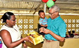 This toddler seem to be getting all the information he needs about his new toy truck from President David Granger while Minister Simona Broomes looks on. (Ministry of the Presidency photo)