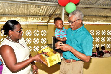 This toddler seem to be getting all the information he needs about his new toy truck from President David Granger while Minister Simona Broomes looks on. (Ministry of the Presidency photo)