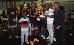 Captain of the Hustlers  and tourney MVP Jermaine ‘Brown Boy’ Scotland (centre) collecting the championship trophy from New Era Co-Director Andrew Major in the presence of teammates and supporters while New Era Co-Director Shareef Major look on.