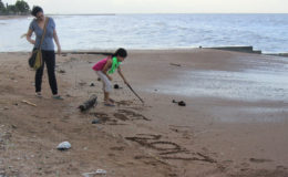  A mother looks on as her daughter writes New Year greetings in the sand at the seawall yesterday. (Photo by Keno George)
