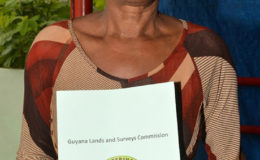Paula Benjamin poses with her ‘Permission to Occupy State Lands’ document, which she received yesterday from Minister of State,  Joseph Harmon (Ministry of the Presidency photo)