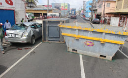 This vehicle (left) was severely damaged yesterday after a Muneshwer’s truck travelling along Lombard Street with a quantity of skip bins became tangled in electrical wires causing one to be dragged off the truck and smashing into the parked vehicle. A man, who was standing near to the vehicle suffered minor injuries. The owner of the parked car is said to be in Linden. (Photo by Keno George)