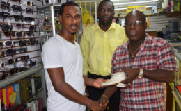 Gregory Richardson (left) collecting his gold chain from Proprietor of Juniors Jewelry Ferdinand Bacchus (right) for being the top scorer in the Ministry of Health/Busta soft shoe football competition while Petra Organization member Clifford Jones looks on.