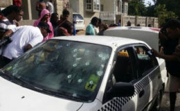 Onlookers scrutinize the bullet-riddled taxi in which the alleged gunmen were travelling.