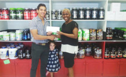 CEO of Fitness Express, Jamie McDonald presenting the GAPF’s General Secretary, Andrea Smith with the financial pact to offset expenses of tomorrow’s juniors and Novices Championship. Also captured in the lenses is little Zoe, a future powerlifter. 