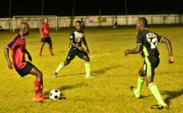 Orville Stewart (left) of Riddim Squad attempting to pass the ball between two players from Mahaica Determinators during their matchup in the 2nd Annual Petra Organization/Limacol Football Championship at the Victoria Ground.