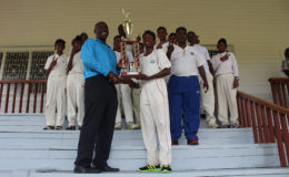 East Coast Under 15 captain Deveanand Khemraj is flanked by his teammates as he collects the champion’s cup from GCB’s Territorial Developmental Officer Colin Stuart. 