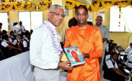 President David Granger receives a copy of a holy text from Swami Shivashankaranandaji (Ministry of the Presidency photo)