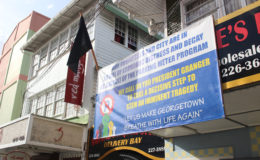 The front of Naraine’s Liquor Store bearing a banner with the slogan “Let us make George-town breathe again with life,” alongside which hangs a black flag. 