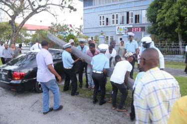 Police officers, assisted by public-spirited citizens, removing a utility pole that broke and fell on a car on Brickdam yesterday, after it was hit by a minibus. (Photo by Keno George)