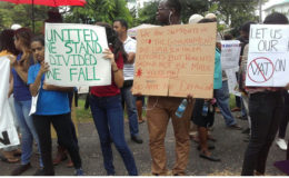 The placard at centre charges the government to go after schools that are in default of their tax payment rather than placing the burden on parents and students. (Photo by Oliceia Simon-Tinnie)