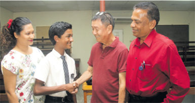 Math teacher Bernard Assing, congratulates student Aaron Mohammed, who earned a distinction in the CSEC math exam. Also in photo are Mohammed’s parents Nazir, right, and Nadia