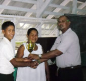 Flashback: Veral Felix, a student of Skeldon High school, receiving his trophy from school teacher Zahir Moakan at the 2015 Berbice Inter-School Chess Championships. Skeldon High won the tournament which was organized by Krishnanand Raghunandan, the Guyana Chess Federation’s Berbice representative. Felix was accompanied by his mother (centre) to participate in the tournament, travelling from his residence in Orealla.