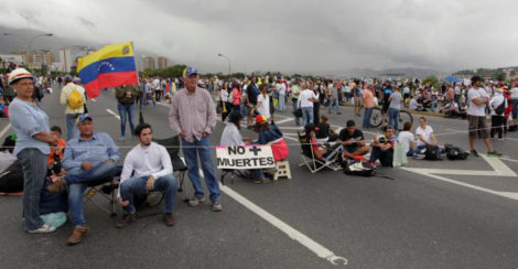Opposition supporters sit next to a placard that reads: ‘No more deaths’, as they block a highway, during a protest against Venezuelan President Nicolas Maduro’s government in Caracas, Venezuela May 15, 2017. (Reuters/Christian Veron)