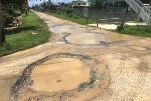 Large potholes filled with water occupy the entire width of one of the roads in Industry 