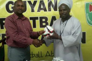 Guyana Football Federation (GFF) president Wayne Forde presents the footballs to one of the organisers of the 10th annual St Romain Memorial games.