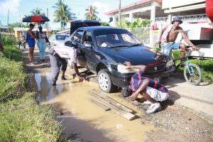 Rescue mission: These men were left to explore options to remove this car which was caught in a pothole on Tuesday along Cactus Road, West Ruimveldt. Stabroek News understands that the pothole has been there for some time and causes much inconvenience to those who traverse the road on a daily basis.  (Keno George Photo) 