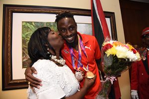 Yvette Wilson,left, plants a kiss on her son, double IAAF World Championship medalist Jereem Richards following his arrival at Piarco International Airport, on Monday.