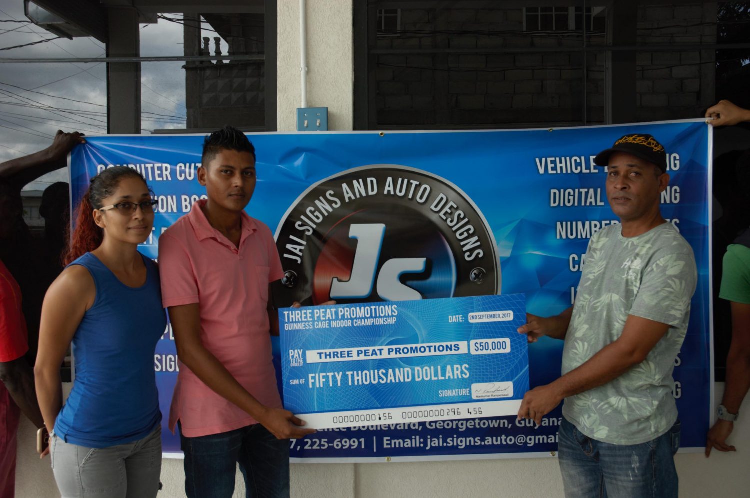 Rawle Welch (right), representative of Three Peat Promotions collects  the sponsorship cheque from Jai Signs and Auto Designs representatives Anjunee Harris and Zaheer Mendonca.