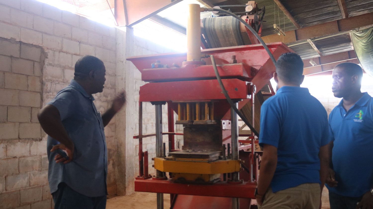Remigrant Robert Cameron (left) demonstrating to CH&PA Chief Executive Office Lelon Saul (far right) and Projects Director (ag) Omar Narine how the calcine and laterite blocks are made.