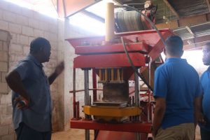 Remigrant Robert Cameron (left) demonstrating to CH&PA Chief Executive Office Lelon Saul (far right) and Projects Director (ag) Omar Narine how the calcine and laterite blocks are made.