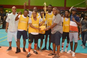 Banks DIH Limited Outdoor Events Manager Mortimer Stewart hands over the championship trophy to Ol Skool Ballers captain Roy Cassou in the presence of his team-mates following their 3-1 win over Future Stars in the Guinness ‘Cage’ Football Championship Saturday night at the National Gymnasium. (Orlando Charles photo)