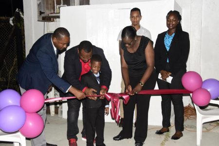 Troy Mendonca (second  from left), Co-Director of the Petra Organization in the presence of Minister of Education Nicolette Henry (third from left) and GFF President Wayne Forde (left), assists his son in cutting the ribbon to unveil the lighting system at the Ministry of Education ground. Witnessing the unveiling is Ansa McAl representative Shawn Abel (second from right)