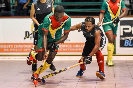 Jamarj Assanah (center) of Guyana in the process of getting dispossessed from his Trinidad and Tobago marker during their clash at the Cliff Anderson Sports Hall, in the Pan American Indoor Hockey Championship
