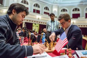 Requiring a draw in the final round to win the 2017 Isle of Man Chess Tournament, World Champion Magnus Carlsen (right), playing the black pieces, worked his way for equality against American grandmaster Hikaru Nakamura (left). In 18 excellent moves the draw was achieved. Carefully observing the game is former world champion Viswanathan Anand (standing). Anand placed second, and Nakamura third. (Photo: Chess.com/Maria Emelianova)