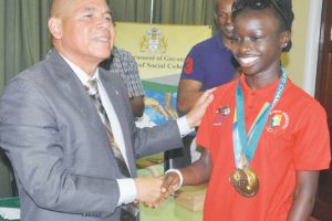 YOU”VE DONE US PROUD HERE”S YOUR NSC MEDAL! Minister George Norton presents Deshawna Skeete with another medal to go with the gold medal she won in the 400m at the recent South American Youth games in  Chile.