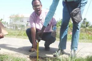 Auditor General Deodat Sharma (stooping)  measures the thickness of the №. 52 Cross Street and Middle Walk access South of Public Road.

