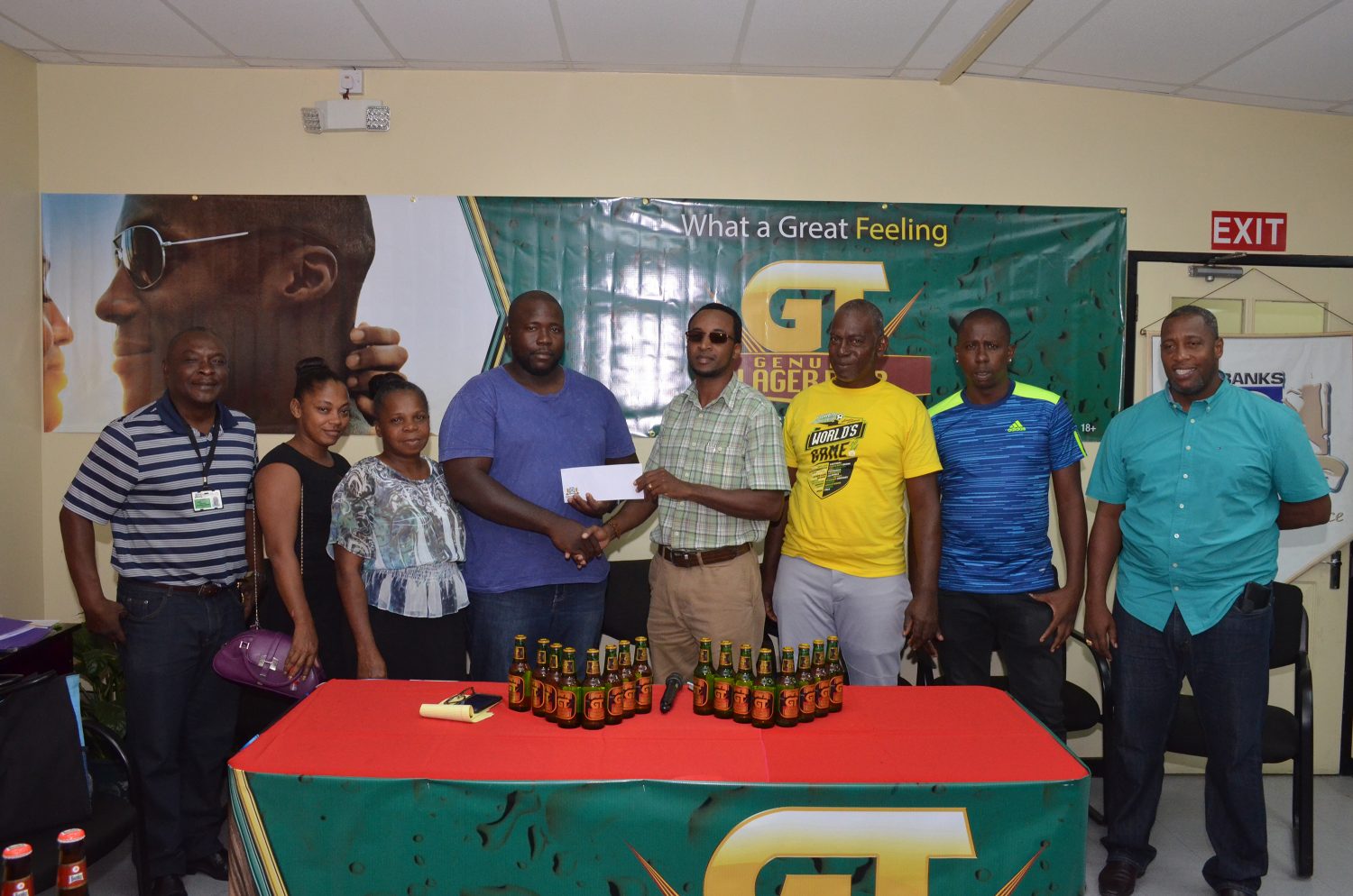 Coach of Den Amstel and tournament host O’Neil Heywood (3rd from left), receiving the sponsorship cheque from Banks DIH Limited GT Beer Brand Manager Jeffrey Clement in the presence of company executives and members of Den Amstel FC