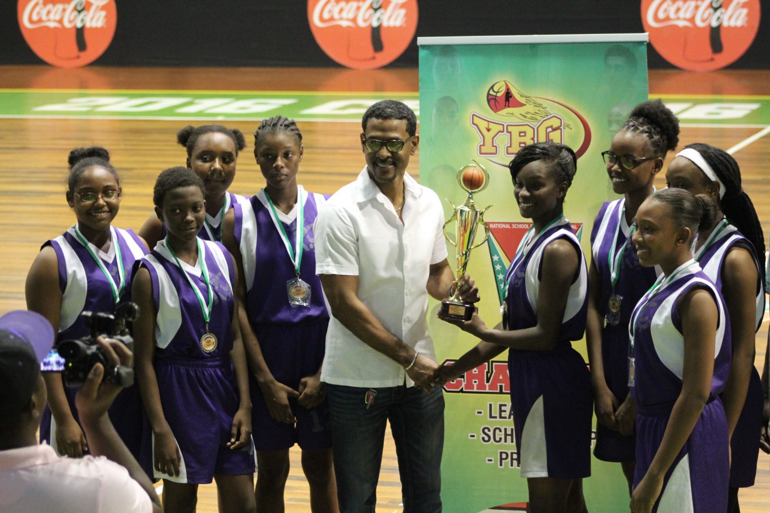 aYBG Co-Director Rayad Boyce handing over the championship trophy to Women’s MVP and Captain of the Victorious President College’s team, Annalisa Barclay, following their narrow win over Marian Academy at the Cliff Anderson Sports Hall