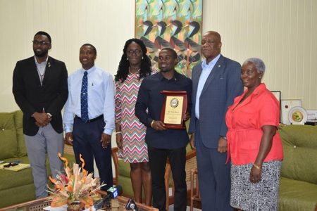 Troy Doris poses with his plaque of achievement from Minister of State Joseph Harmon while in the presence of Director of Sports Christopher Jones, Permanent Secretary of the Ministry of Public Service, Reginal Brotherson (second from left) and other MOTP Staff.
