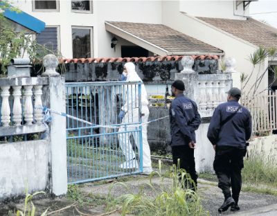 Police officers attached to the Northern Division Task Force East look on as a crime scene investigator searches for evidence at the home of Chinese businessman Qumehlanj Cao on De Graff Street, Arima yesterday.