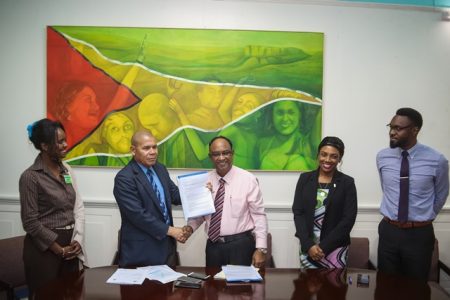 Minister of Social Cohesion, Dr. George Norton (second from left) receiving the agreement from Guyana Amazon Warriors Operation Manager, Omar Khan. (DPI photo)