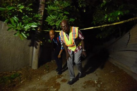 INDECOM investigator Floyd McNabb (right) along with a policeman cross the crime scene tape. (Jamaica Gleaner photo)
