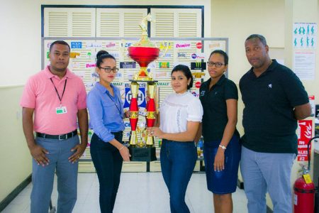 Banks DIH Limited representative Shenisa Fredericks hands over the Championship Trophy to Alisha Mohamed of the organizing committee while Mortimer Stewart, Rawle Nedd (Banks Beer Manager) and Dennisa Paton look on.
