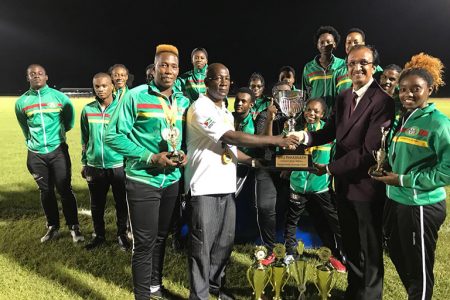 The triumphant University of Guyana Team coach Mark Scott (second from left, front row) receives the Brij Parasnath National College Athletics Championships Trophy from Brij Parasnath (second from right). Champion Male athlete Osafa Dosantos is at extreme left while Champion Female Athlete, Ruth Sanmoogan is at extreme right.