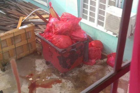 A dumpster overflowing with bags of medical waste in the hospital’s compound. Blood can be seen leaking along the ground.