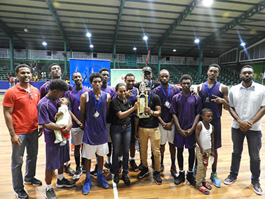 The Victorious LTI unit posing with their spoils after defeating Mackenzie High to retain the u19 championship in the NSBF at the Cliff Anderson Sports Hall. Also in photo are Director of Sport Christopher Jones (right) and YBG Co-Director Rayad Boyce