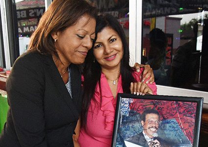 :‘We got our justice’: Lisa McKenzie, right, holding a picture of her deceased husband, Ricardo McKenzie, is embraced by her sister-­in-law, Ingrid McKenzie, on Saturday at Lisa’s Woodbrook business place, Smokey & Bunty on the Avenue. 