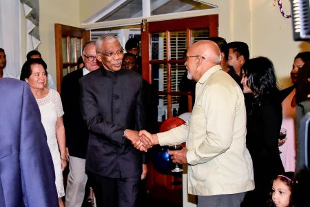 President David Granger (centre) greeting former President Donald Ramotar at the French National Day observance last evening at Cara Lodge. (Ministry of the Presidency photo)