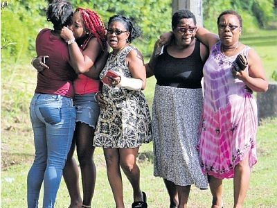 Shaquille Patrick’s mother Rosey, second from right, is consoled by relatives while nieces of Romell Goodridge embrace each other at the accident scene along the Valencia Stretch yesterday.