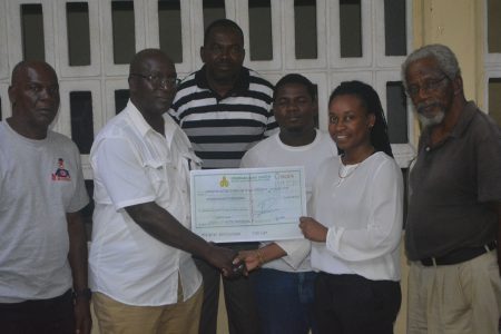 Businessman Lloyd Britton presenting the cheque to Chairperson of the BV/Triumph 8th of May group, Latecia Stuart, in the presence of other executive members.
