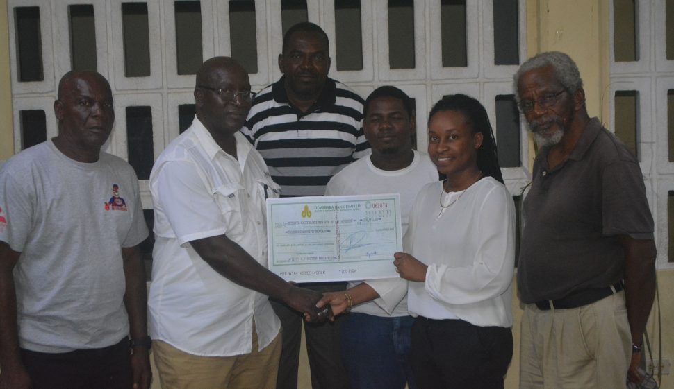 Businessman Lloyd Britton presenting the cheque to Chairperson of the BV/Triumph 8th of May group, Latecia Stuart, in the presence of other executive members.