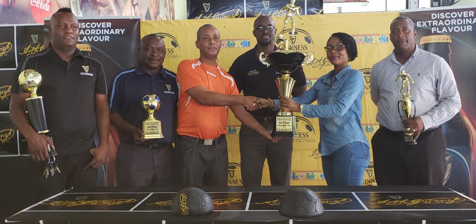 Tournament coordinator and principal of Three Peat Promotions Rawle Welch (3rd from left), collecting the championship trophy from Colours Boutique representative Samantha Thomas in the presence of (left to right)Referees Coordinator Wayne Griffith, Banks DIH Communications Director Troy Peters, Guinness Brand Manager Lee Baptiste, and Banks DIH Outdoor Events Manager Mortimer Stewart
